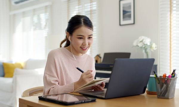 Asian female attending a webinar, writing in her notepad