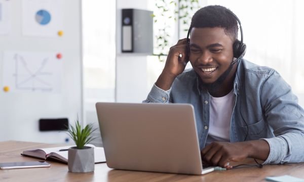 African American worker wearing headphones, watching webinar on laptop in office