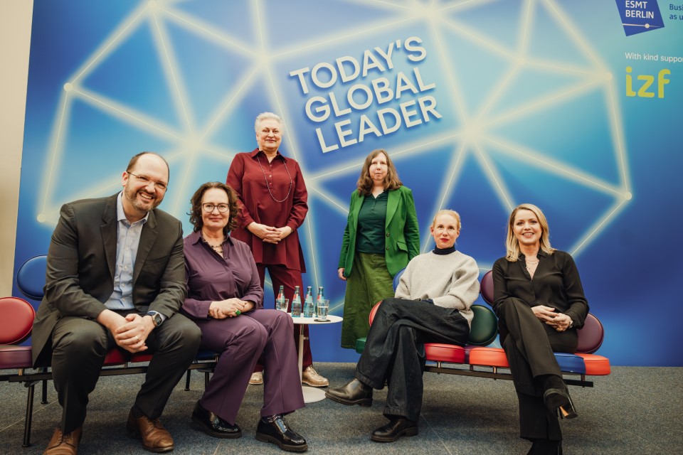 Six speakers at a panel discussion seated and standing in front of a blue backdrop reading “Today’s Global Leader,” with ESMT Berlin and izf logos visible.