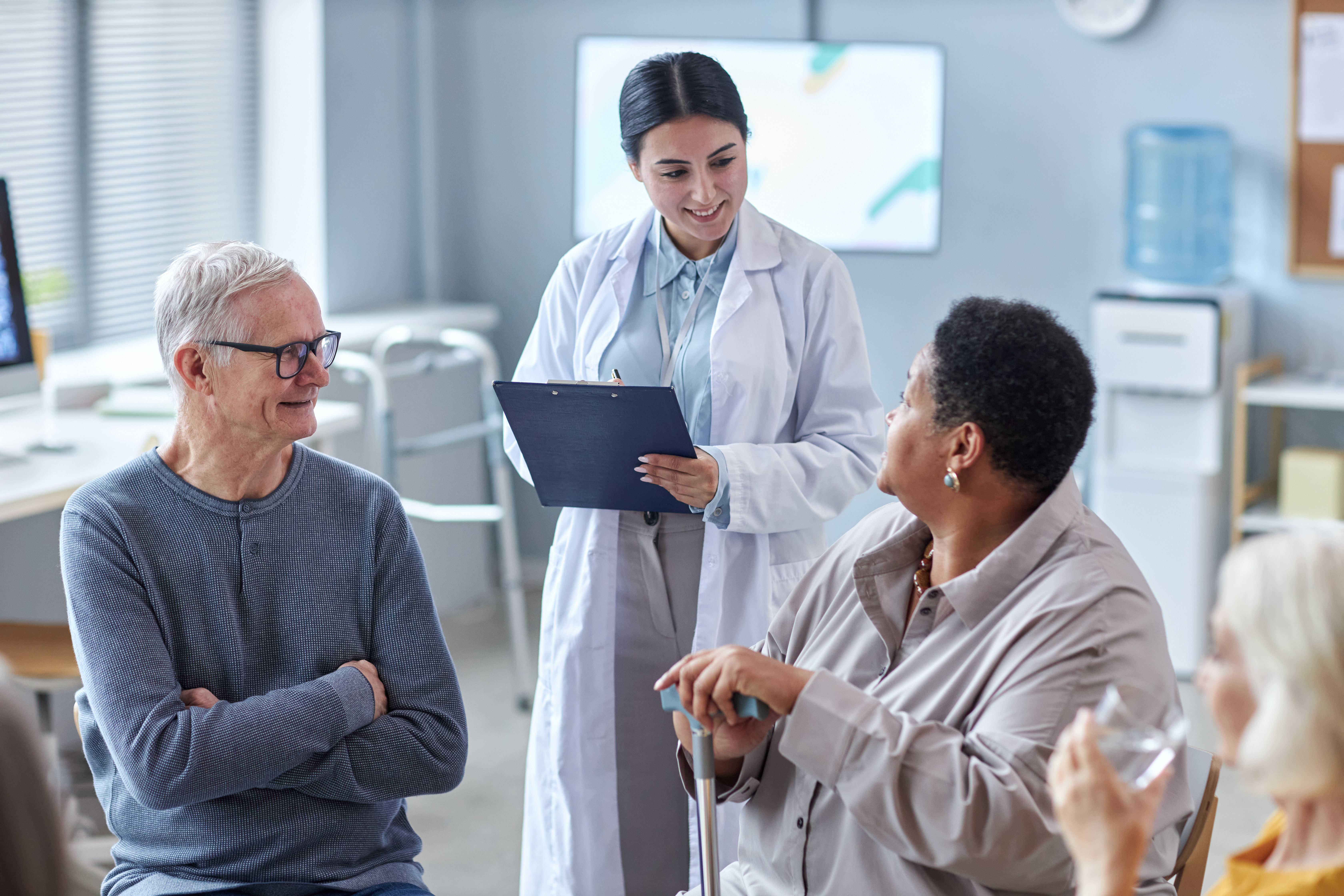 Doctor speaking with a group of older adults during a support group or consultation in a medical office.