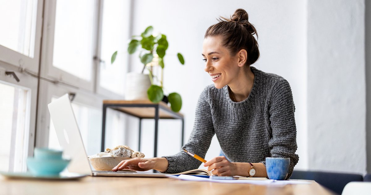 Woman in a grey sweater watching an online webinar while having breakfast at home