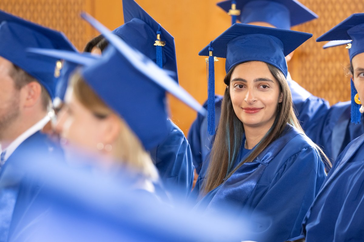 An ESMT MBA graduate in a blue cap and gown, smiling with her cohort at their MBA graduation ceremony
