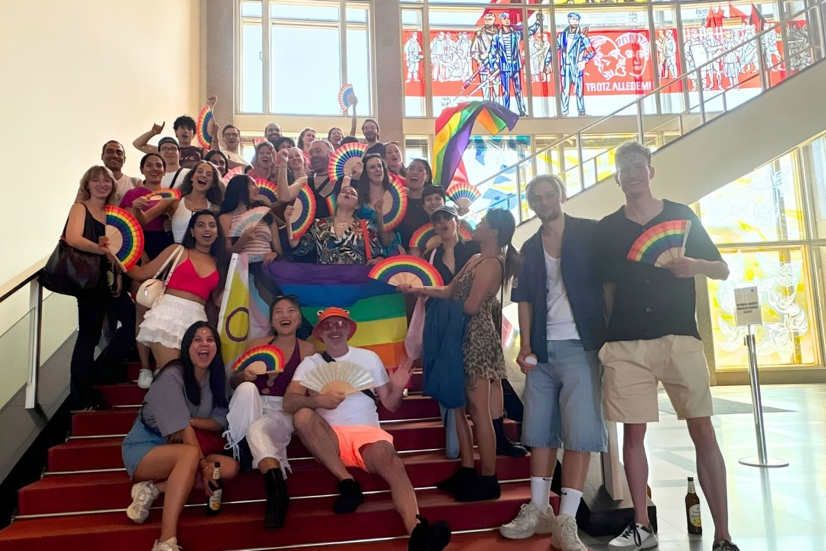 Students from the ESMT Pride Impact club posing for a group photo on campus. They have rainbow flags and fans.
