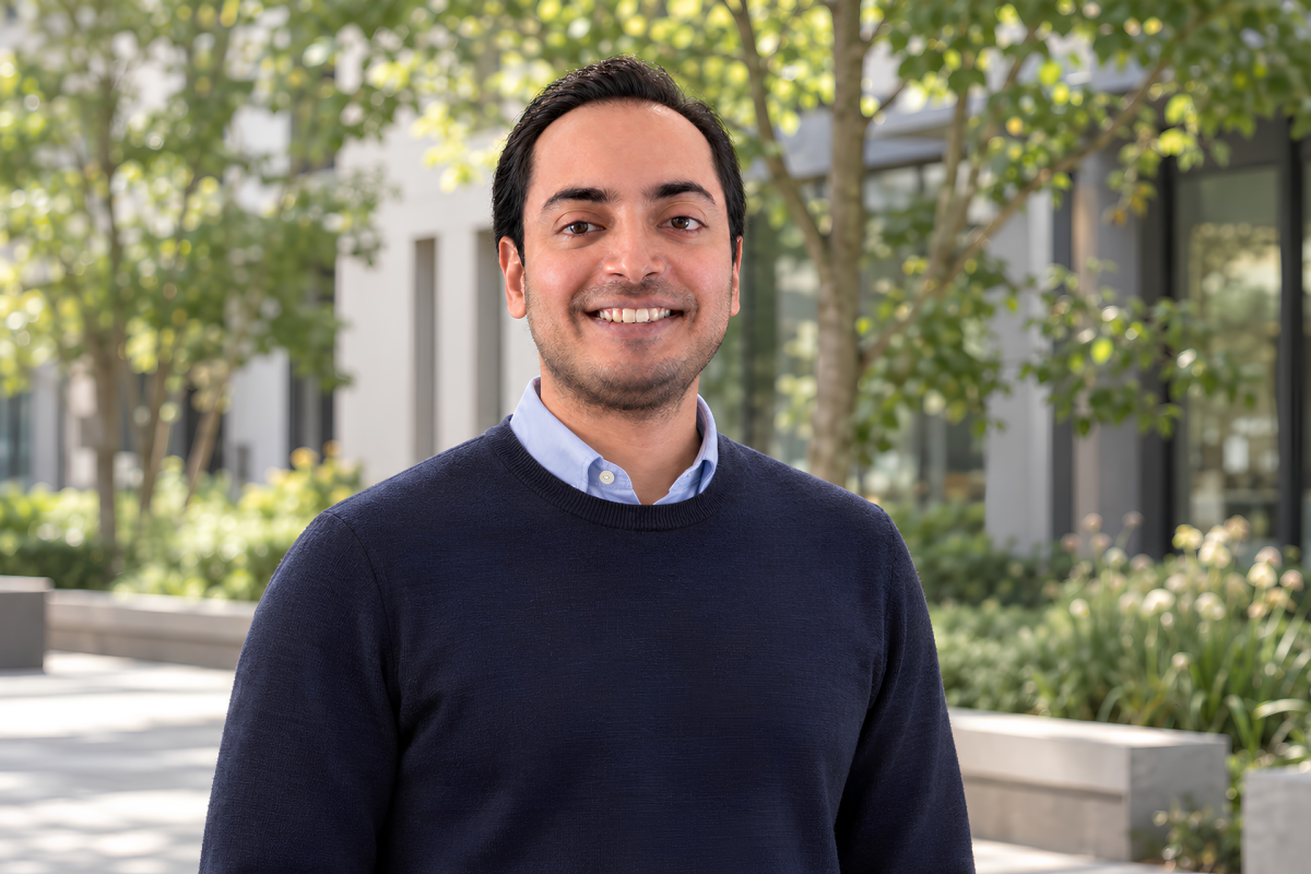 Portrait of ESMT Berlin Full-time MBA alum Animesh Srivastav standing outside on a summer day. He is wearing a blue sweater and smiling.