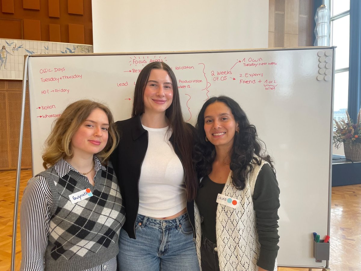 ESMT Berlin Master in Innovation and Entrepreneurship students Jasmin Mantwill, Laura Ruiz, and Gwyneth-Tyger Carys Neumann standing in front of a whiteboard brain-storm while working on their app Lunara