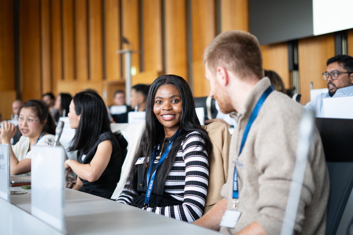 ESMT Berlin Global Online MBA student Joan Mwaniki and her cohort on campus for Berlin Experience Week. They are sitting in a lecture hall and smiling at the camera