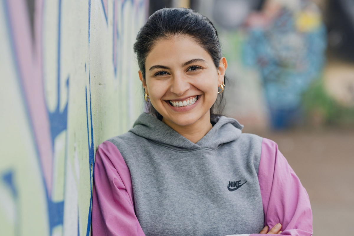 ESMT Berlin Full-time MBA alum Farah Nafi' standing by a graffitied wall in central Berlin and smiling