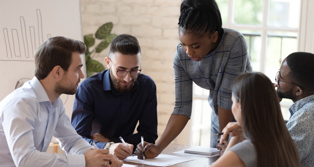 Diverse group of people at an office meeting looking at paper on table