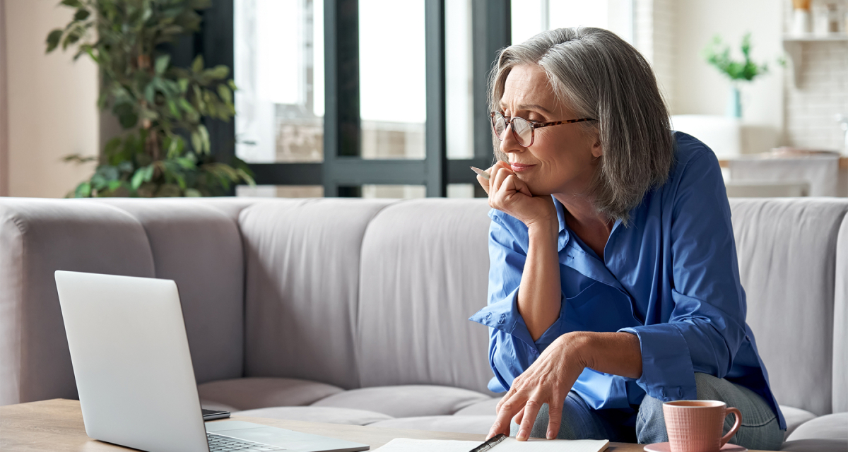 Woman sitting on couch working on laptop placed on coffee table. 