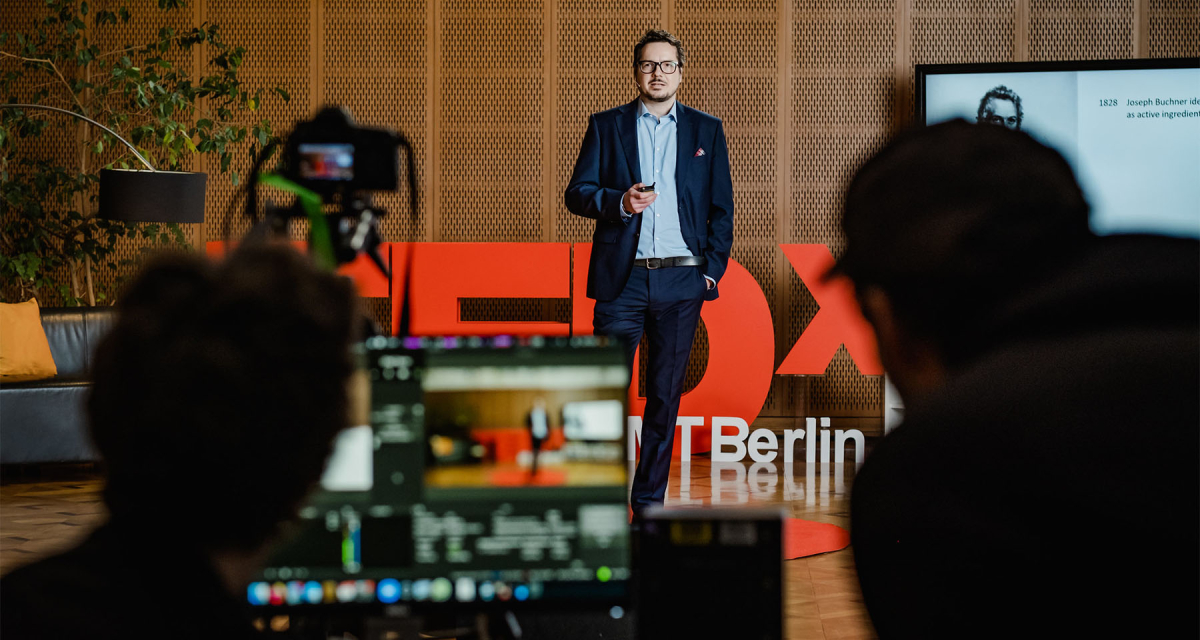 Stefan Wagner speaking at TEDx event at ESMT with blurred view of camera and camera man in front of the stage 