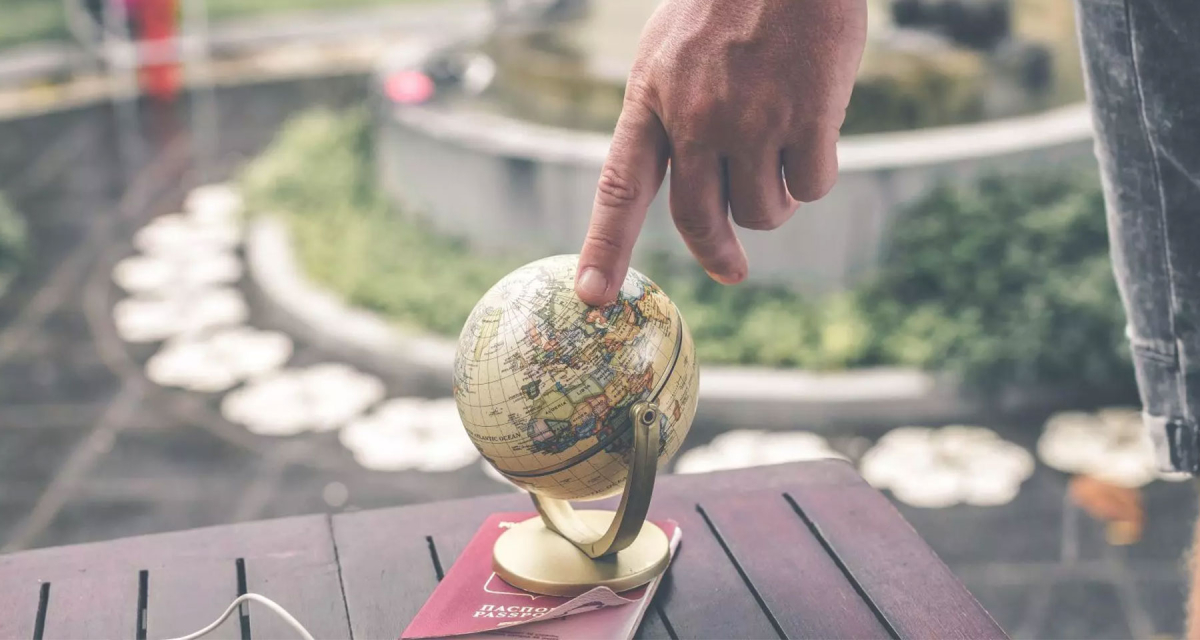 A person's hand touching a small globe atop a passport