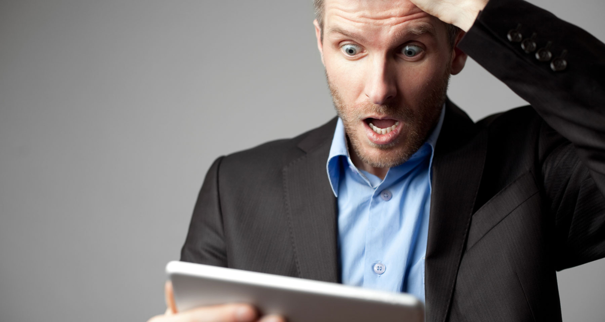 Whie male in a business suit with a shocked expression on face looking at tablet. 