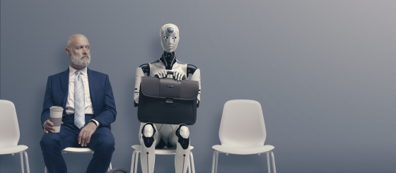 A white male in a business suit and a robot are sitting next to each other waiting for a job interview
