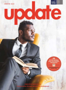 Black man wearing suit sittin on yellow armchair with open book in hands, looking to the left