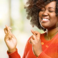 Smiling black woman crosses her fingers for luck