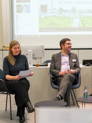 Panel discussion with four participants seated on stage at the ESMT Coaching Colloquium, engaged in conversation in front of a presentation screen.