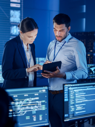 Two people working in a room filled with multiple monitors and computers, focused on their tasks.