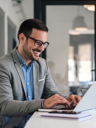 Cheerful male professional working on laptop while sitting at office desk
