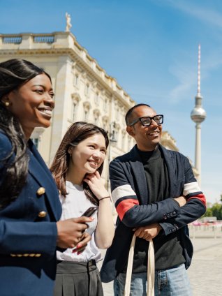 Group of young professionals smiling and talking outdoors in central Berlin, with the TV Tower in the background.