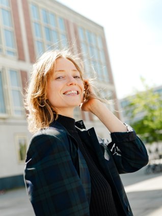 Picture of Johanne Björklund Larsen, an ESMT Berlin Full-time MBA student, standing outside the campus building in the sunshine and smiling. 