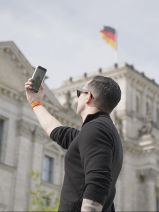 An ESMT Berlin Full-time MBA student taking a picture of the Bundestag in Berlin on his phone. The German flag is visible at the top of the building