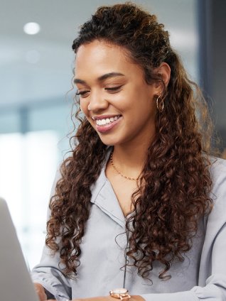 New graduate watching a webinar in her office. She is dressed professionally, and has long, slightly curly hair.