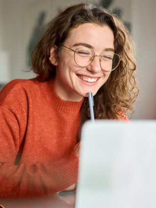 Smiley young woman beaming at the camera and taking notes during a webinar