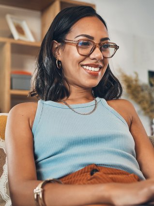Woman in her late thirties with glasses and a big smile. She is sitting on her sofa and watching a webinar on her laptop from the comfort of home