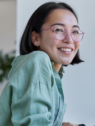 Woman in her twenties looking up from her laptop and smiling. She has pink glasses and a mint green shirt