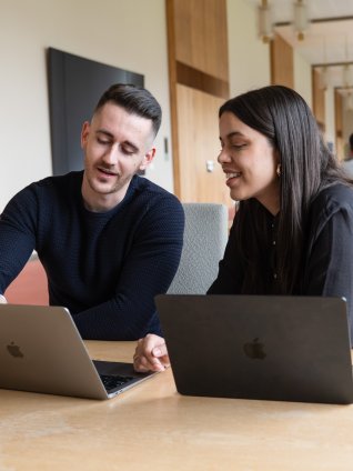 Two students on the ESMT Berlin campus discussing work on their laptops