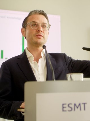 Prof. Michael Weber speaking at a podium at ESMT Berlin during a research presentation.