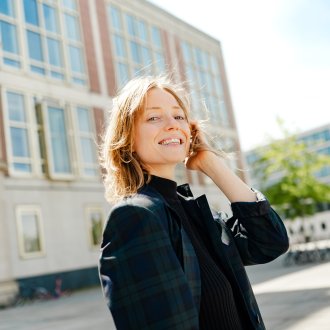 Picture of Johanne Björklund Larsen, an ESMT Berlin Full-time MBA student, standing outside the campus building in the sunshine and smiling. 