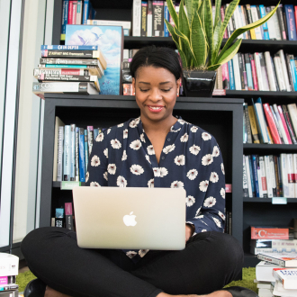 woman sitting on the floor with laptop surrounded by books 