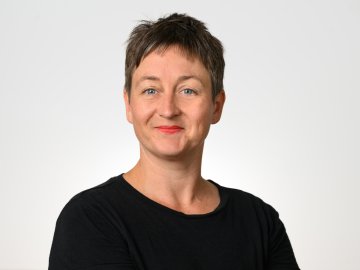 Studio headshot of a smiling woman with short hair, wearing a black top on white background