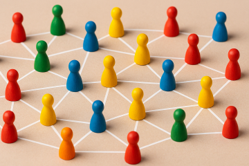 A photograph captures a vibrant network of multicolored wooden meeples, connected by crisp white lines against a neutral beige background. 