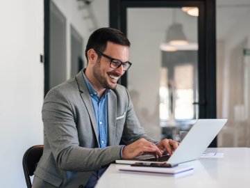 Cheerful male professional working on laptop while sitting at office desk