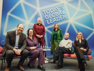 Six speakers at a panel discussion seated and standing in front of a blue backdrop reading “Today’s Global Leader,” with ESMT Berlin and izf logos visible.