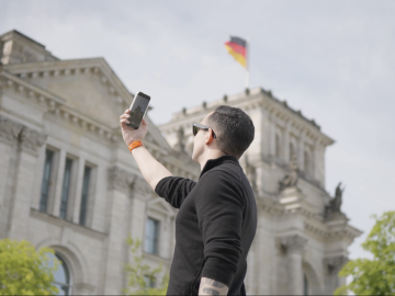 An ESMT Berlin Full-time MBA student taking a picture of the Bundestag in Berlin on his phone. The German flag is visible at the top of the building