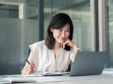 Business woman in her 40s watching an online webinar in the office and taking notes