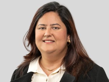 Portrait of a woman with shoulder-length dark hair, wearing a white blouse and black blazer against a light background.