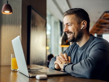 Man in his thirties watching a webinar in a cafe. He is wearing headphones and looking engaged with the topic