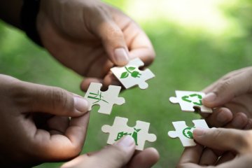 Hands holding puzzle pieces with green sustainability icons, including wind energy, recycling, nature, and the planet.