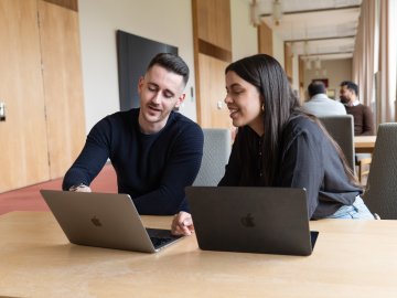 Two students on the ESMT Berlin campus discussing work on their laptops