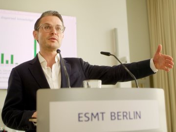 Prof. Michael Weber speaking at a podium at ESMT Berlin during a research presentation.