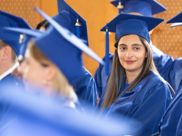 An ESMT MBA graduate in a blue cap and gown, smiling with her cohort at their MBA graduation ceremony