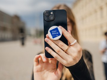 A business school student taking a selfie with an ESMT-branded pop socket on her phone