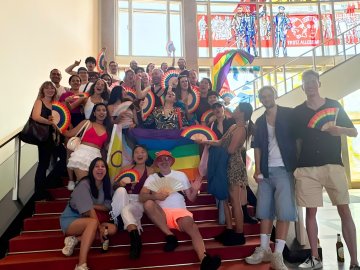 Students from the ESMT Pride Impact club posing for a group photo on campus. They have rainbow flags and fans.