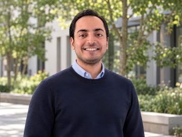 Portrait of ESMT Berlin Full-time MBA alum Animesh Srivastav standing outside on a summer day. He is wearing a blue sweater and smiling.
