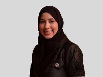 Portrait of Dr. Doaa Farid smiling and wearing a black hijab against a light grey background.