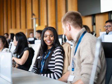 ESMT Berlin Global Online MBA student Joan Mwaniki and her cohort on campus for Berlin Experience Week. They are sitting in a lecture hall and smiling at the camera